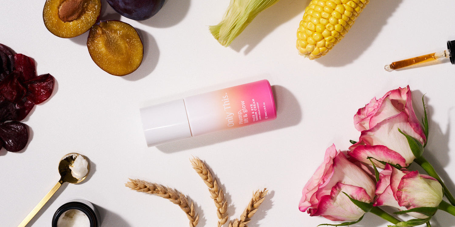 Cosmetic bottle with gradient design surrounded by fruits, vegetables, and flowers on a white surface