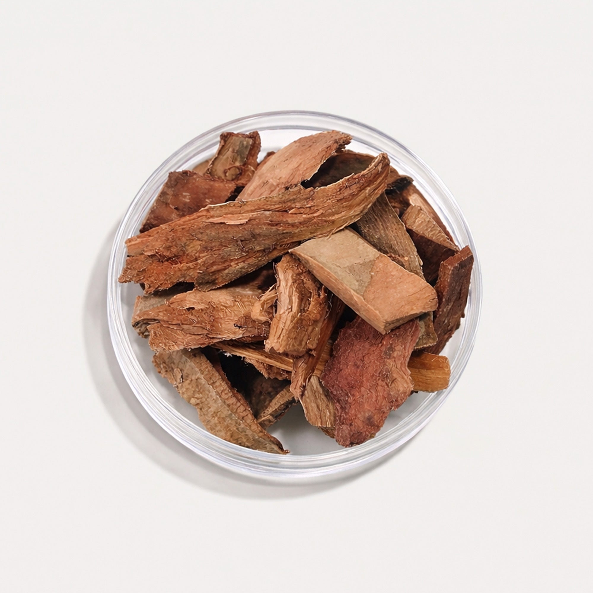 Dried wood chips in a clear glass bowl on a light gray background
