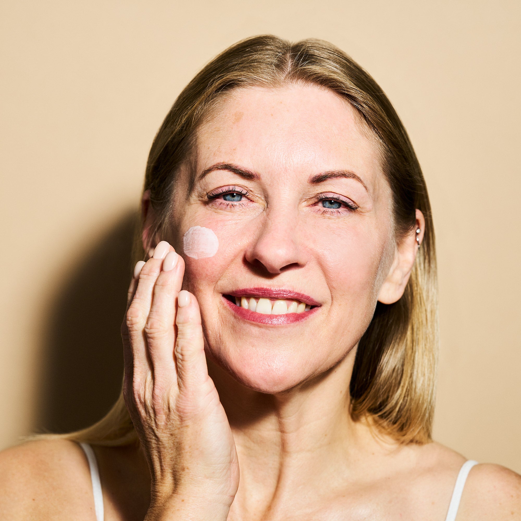 Woman applying cream to her face against a beige background