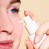 Person applying a white cream to their eye with a applicator against a beige background
