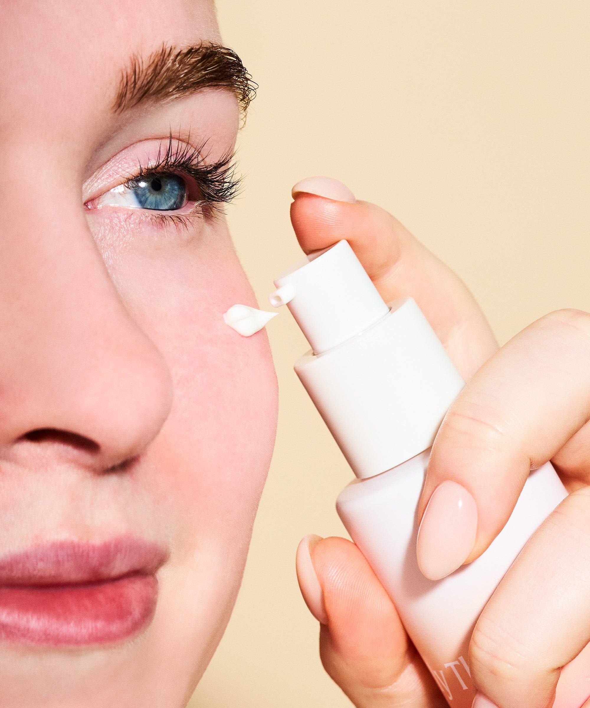 Person applying a white cream to their eye with a applicator against a beige background
