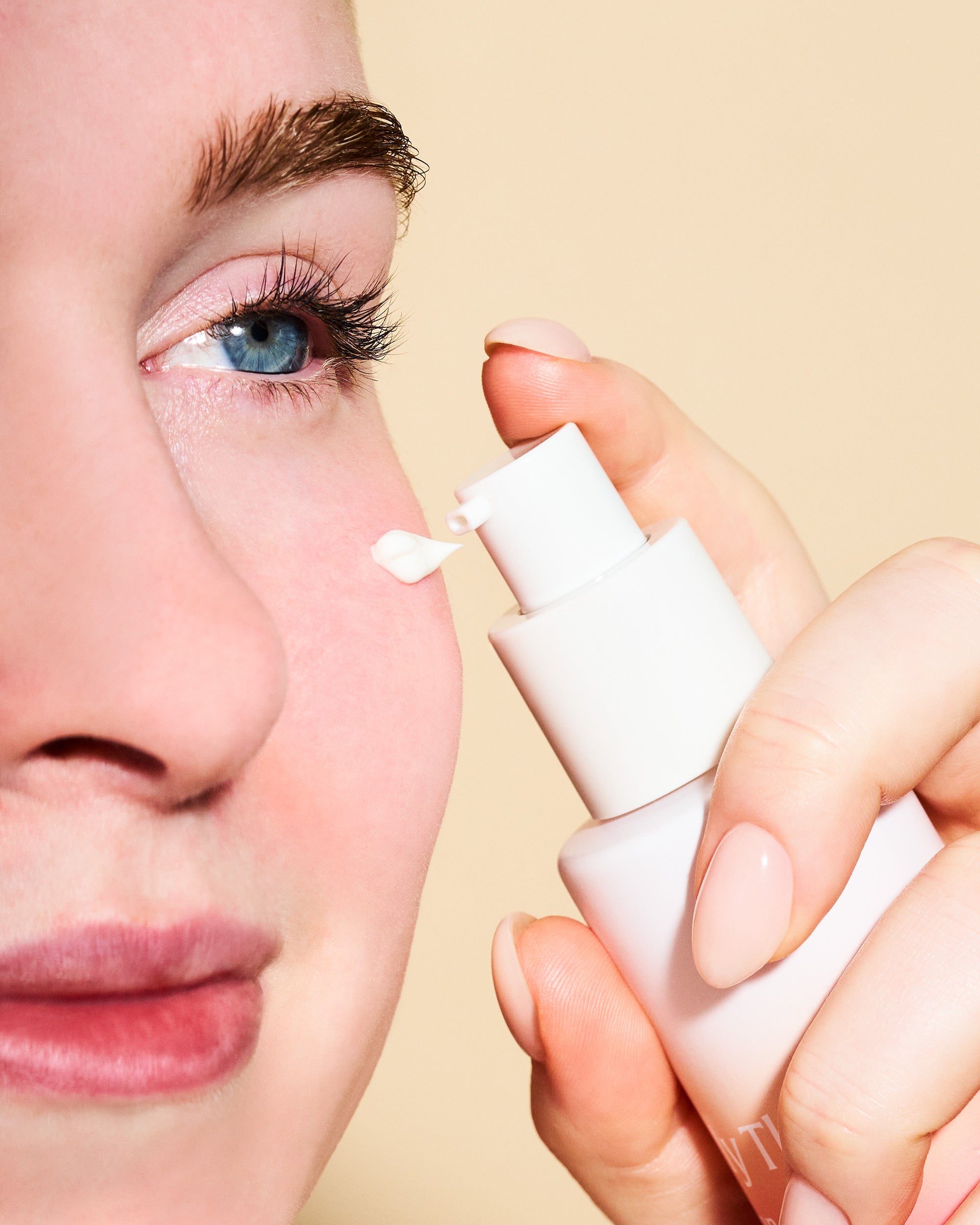 Person applying a white cream to their eye with a applicator against a beige background